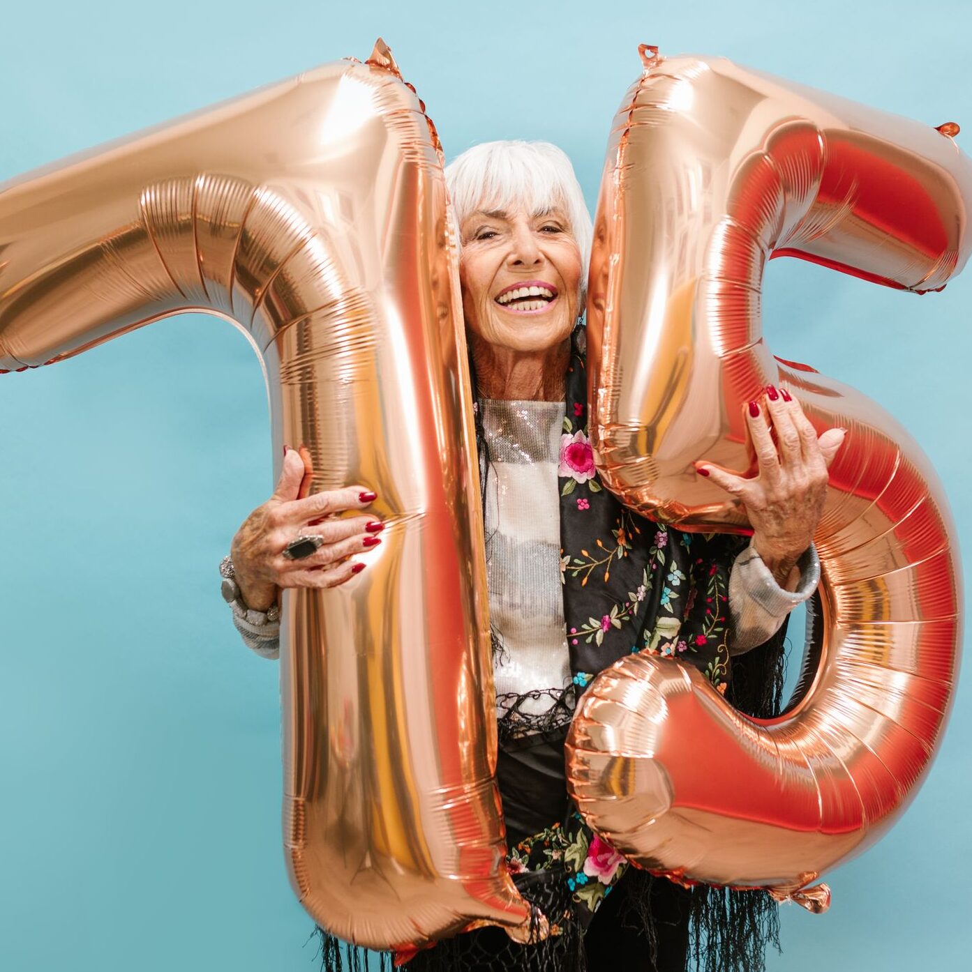 75th Birthday Gifts for Mom: 13 Thoughtful Ideas She’ll Truly Feel 1 Happy senior woman holding 75 balloons on blue background.